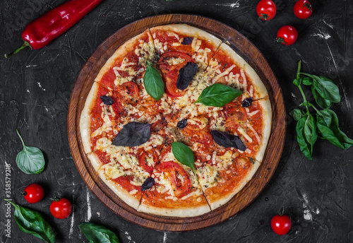 Perfect pizza margarita with tomato slices, basil on a dark background.