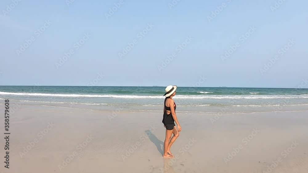 Asian women wear hats and black dresses are Walking and the waves of the sea hitting the sandy beach. Asian women wear hats and black dresses are Walking and the waves of the sea hitting the sandy beach.