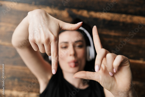 Photo of young woman wearing headphones doing photo frame gesture on floor