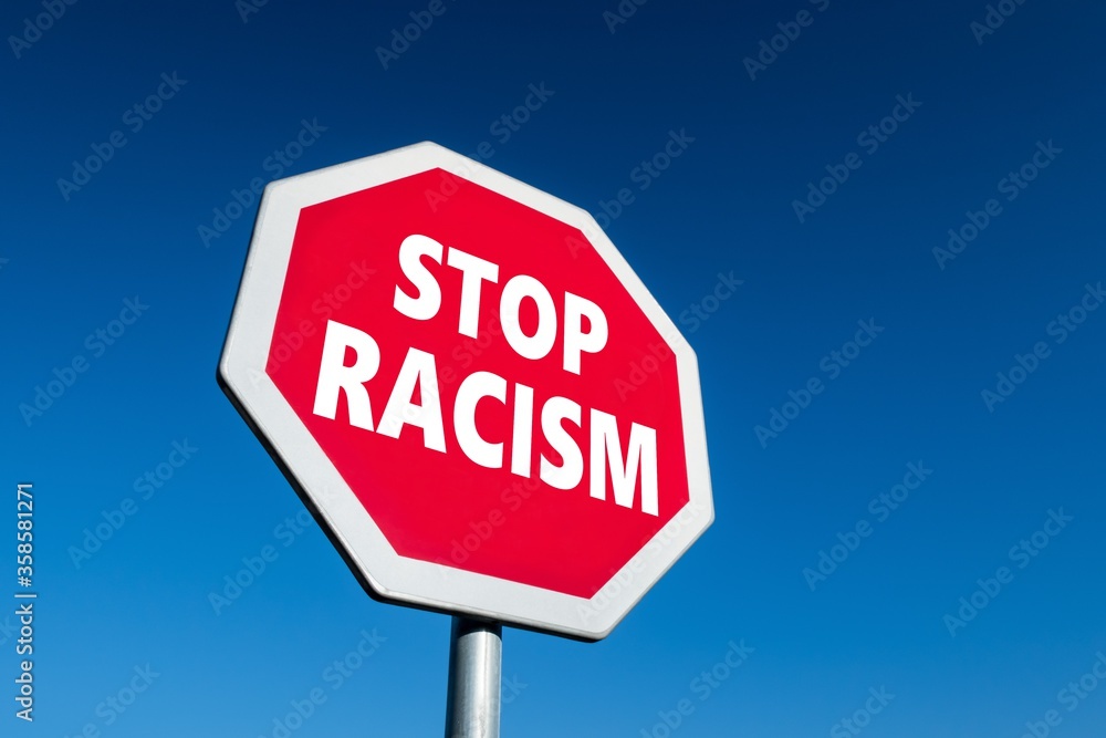 Stop sign with STOP RACISM text in perspective view against blue sky as a reaction for violent activities Stop sign with STOP RACISM text in perspective view against blue sky as a reaction for violent activities