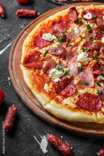 Meat pizza with salami, ham, chicken, sausages and feta cheese, on a blackboard and on a dark background