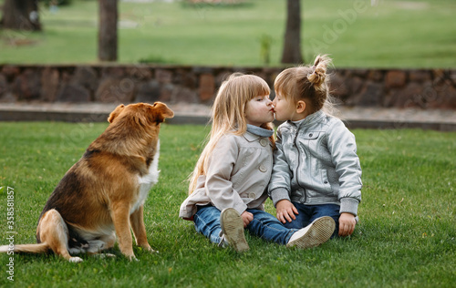 a happy family. little sisters kiss and laugh in the summer outdoors. A dog is sitting nearby © Andrei Sasin