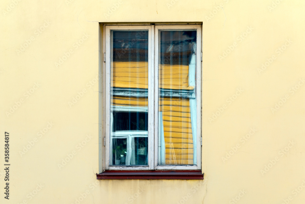 Detail of traditional east european yellow building in a middle window reflection buildings in the sunny day