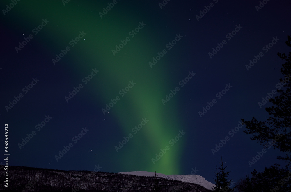 strong aurora borealis, northern light emerging over snowy mountain peak in winter