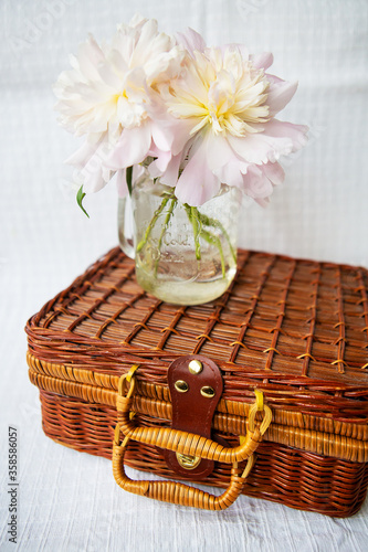 A very beautiful bouquet of pink peonies in a vase stands on a wooden suitcase.