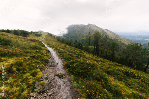 Calm countryside landscape with wet trail and country road with car in distance leading among green mountain hills covered with fog in overcast weather in summer day photo