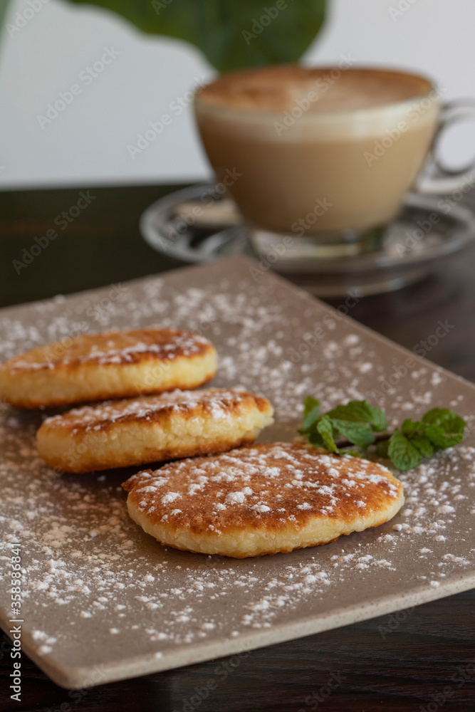 Traditional syrniki or cottage cheese pancakes and cappuccino on a dark table. Russian breakfast, wooden table