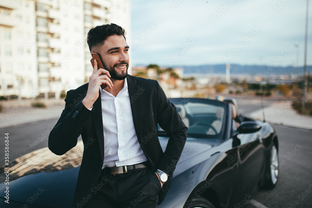 Side view of businessman talking on the phone outside a convertible car. Side view of businessman talking on the phone outside a convertible car.