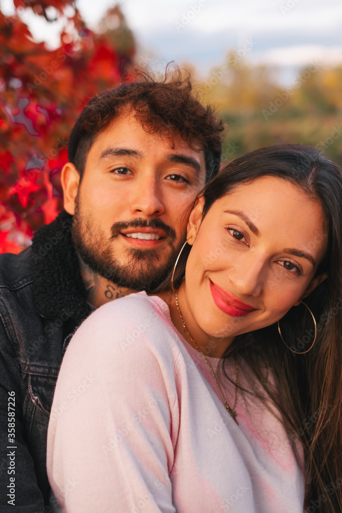 Happy young man and woman embracing while sitting on bench near colorful autumn tree in park Happy young man and woman embracing while sitting on bench near colorful autumn tree in park
