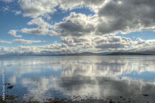 reflective fjord, blue sky, clouds and snowy mountain in summer