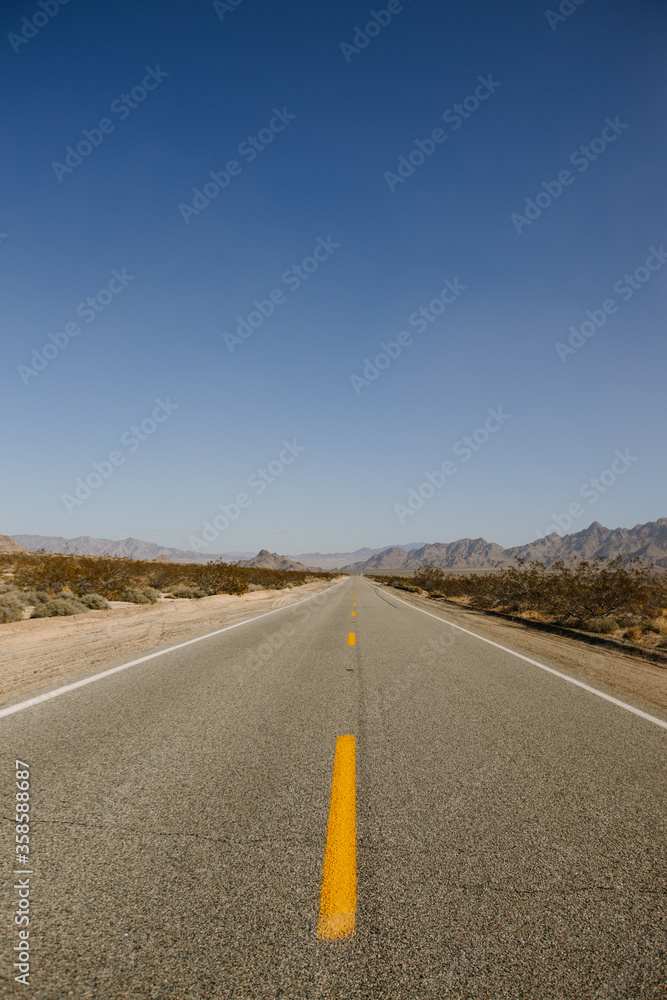 Straight asphalt road going through sandy terrain with dry grass and mountains on background of cloudy sky on heat day in California Straight asphalt road going through sandy terrain with dry grass and mountains on background of cloudy sky on heat day in California