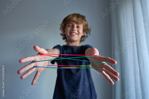 Excited schoolboy in pajamas creating difficult figure with string while playing cats cradle game at home photo