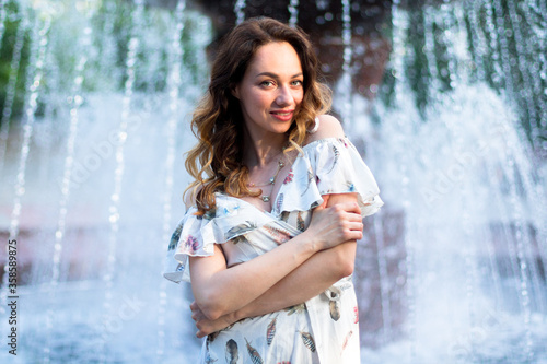caucasian girl in white dress with flowers feels happy near big fountain on the background