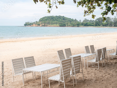 White tables under trees on the beach. Copy space provided.