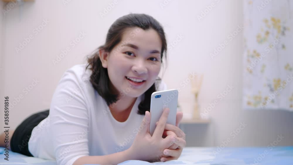 Thai asian woman looking and touching smartphone relax enjoy and smile with online social media in bedroom. Thai asian woman looking and touching smartphone relax enjoy and smile with online social media in bedroom.