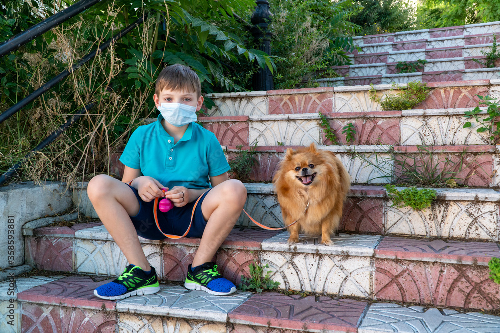 Coronavirus covid-19 concept. A little children boy in a medical mask walks with a dog. Children wearing medical face mask outdoor. New reality.