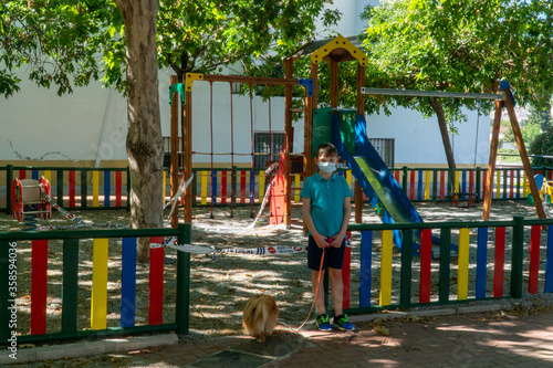 Obraz na płótnie A sad child is standing at the quarantined children's playground. COVID-19 security and protection measures in the city park. w salonie