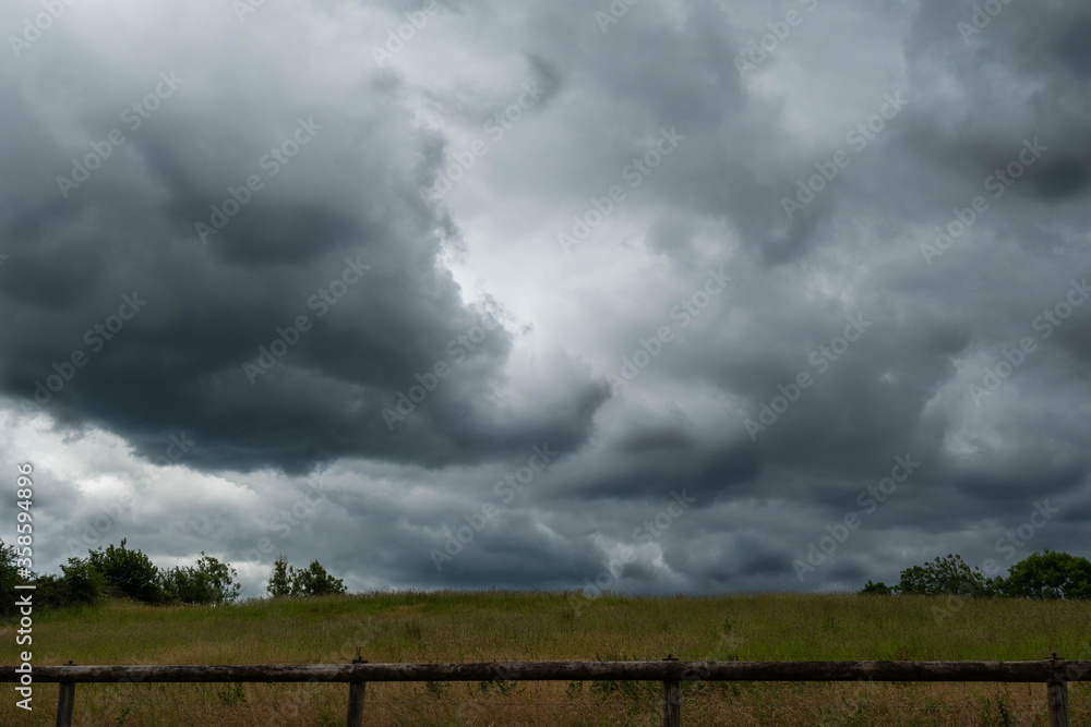 Thunderous dark and moody clouds in the sky over a countryside landscape with fields and trees below 