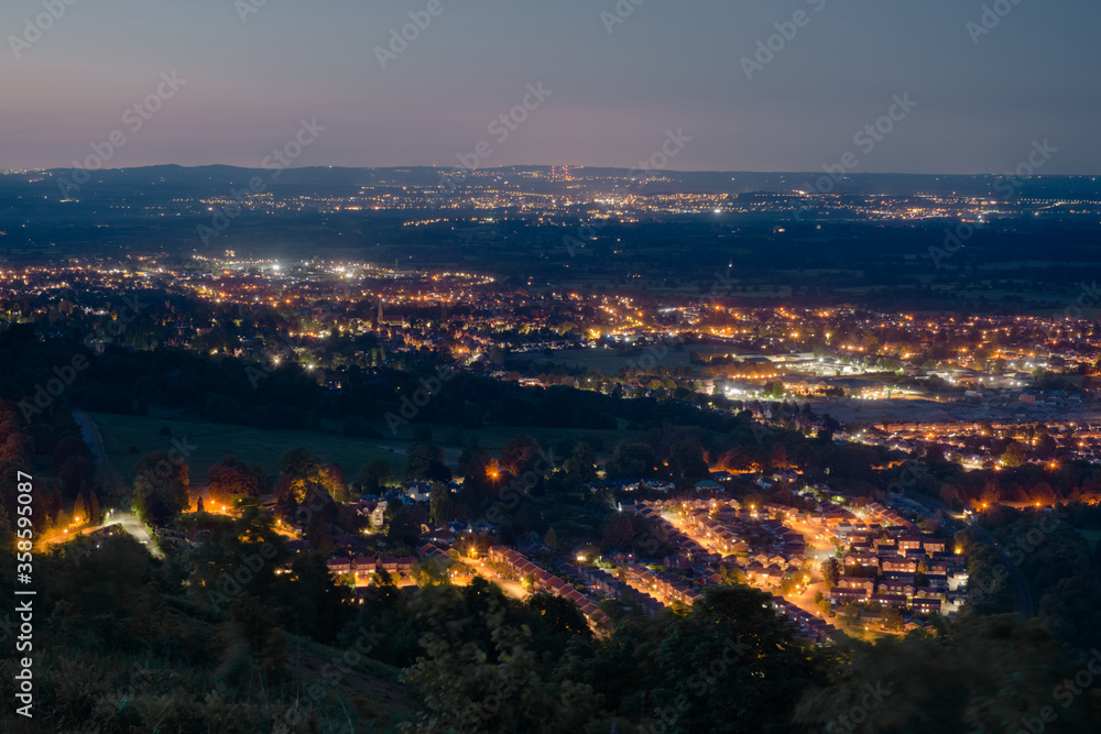 Dusk or night time landscape over small british town Malvern, showing street lamps, and denser populations in the distance.