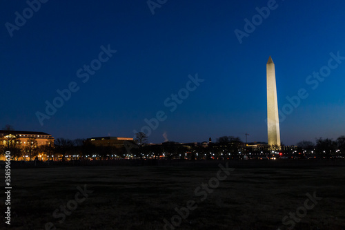 Tall high Washington Monument memorial in blue sky at evening night in winter, lawn, illuminated bright lights dark in December