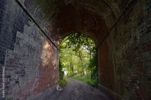 Red brick tunnel contains a muddy double-track lane that opens out into deciduous forest greenery.