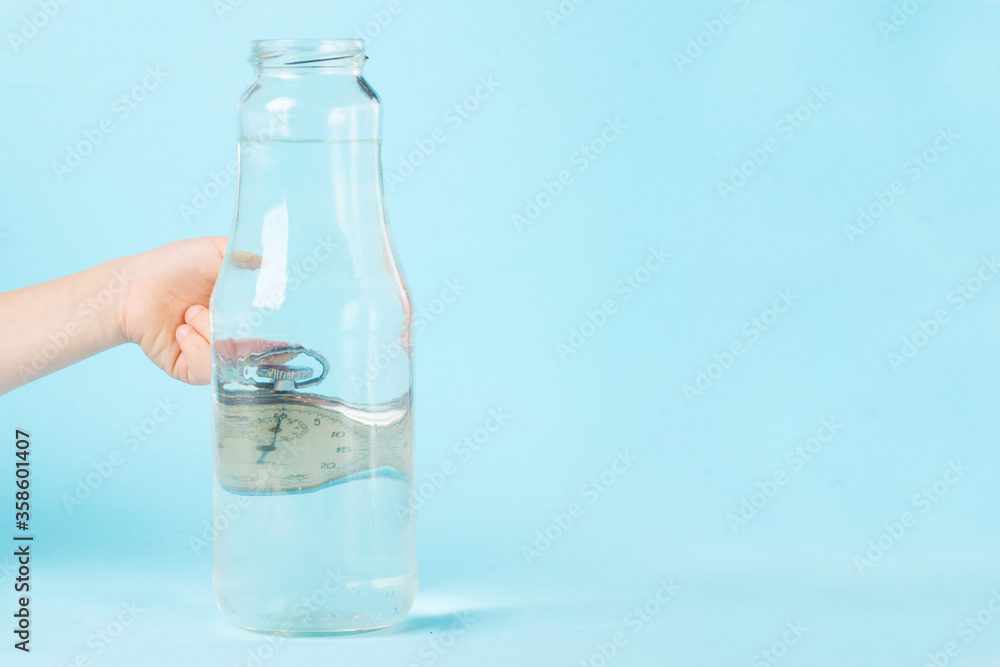 distorted glass of water, watch distorted by liquid water and glass on a blue background, the concept of time warp. distorted glass of water, watch distorted by liquid water and glass on a blue background, the concept of time warp.