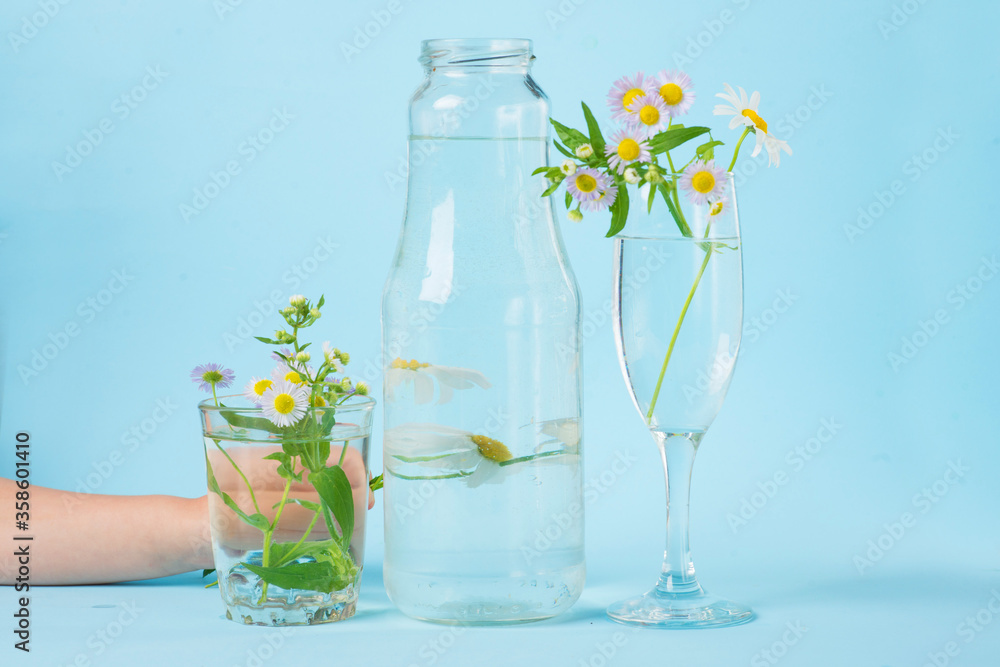 distorted glass of water, flowers distorted by liquid water and glass on blue. distorted glass of water, flowers distorted by liquid water and glass on blue.