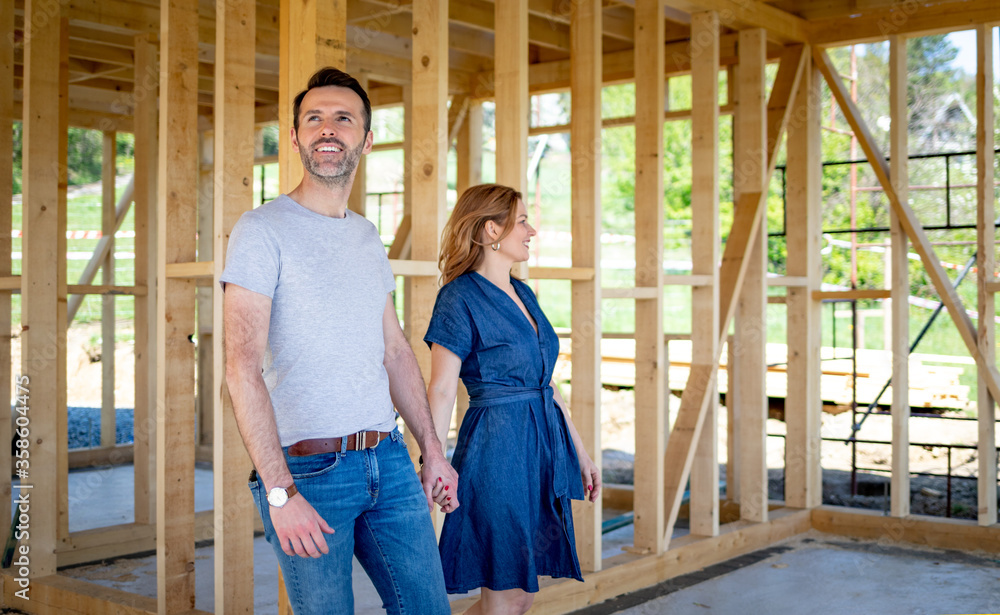 Wife and husband visiting building site of their new house with construction in background Wife and husband visiting building site of their new house with construction in background