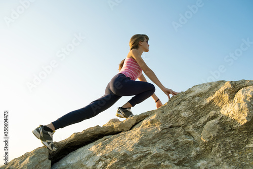 Woman hiker climbing steep big rock on a sunny day. Young female climber overcomes difficult climbing route. Active recreation in nature concept.