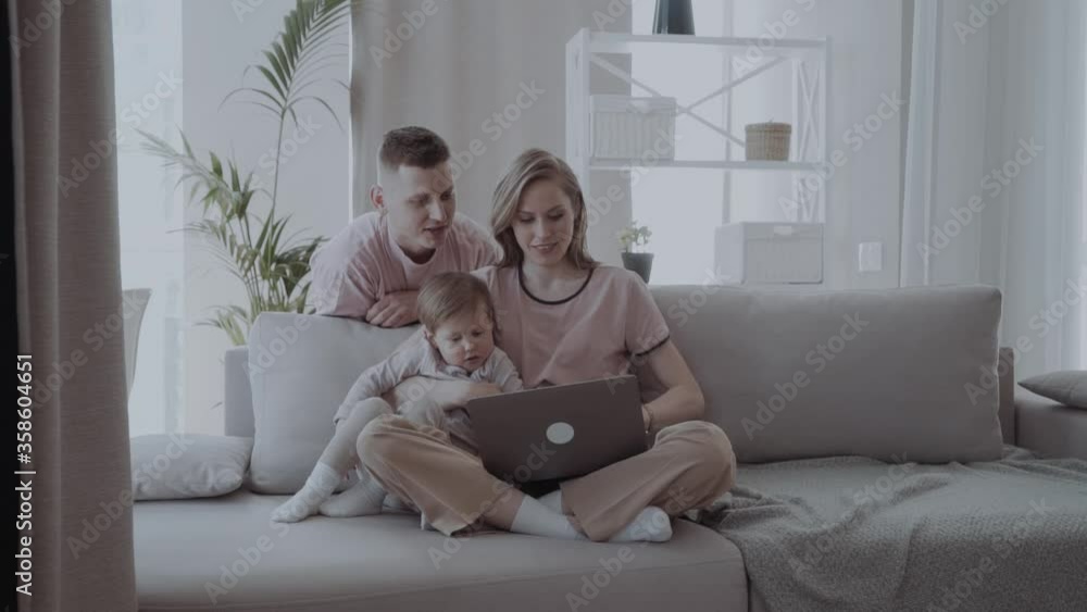 Happy family with kids using laptop sitting on sofa at home, smiling parents and son relaxing on couch holding computer, man woman with childr shopping together online in cozy living room Happy family with kids using laptop sitting on sofa at home, smiling parents and son relaxing on couch holding computer, man woman with childr shopping together online in cozy living room
