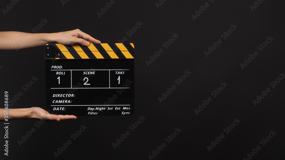 Hand is holding Black with yellow color clap board or movie slate  with number on black background.