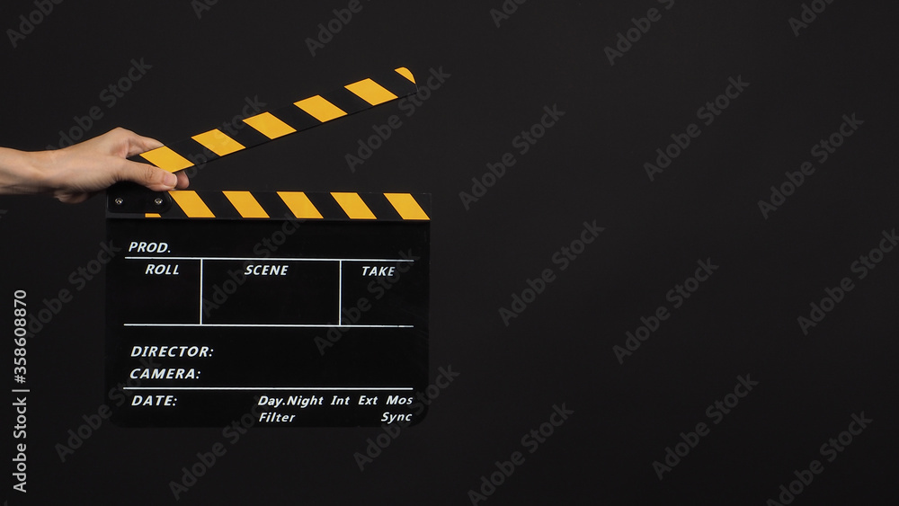 A hand is holding black with yellow color clapper board or movie slate use in video production and film industry on black background.