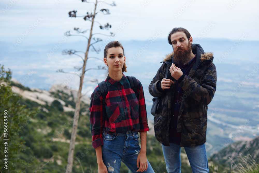 Young couple of hikers with backpacks standing on mountain hill with amazing view on background