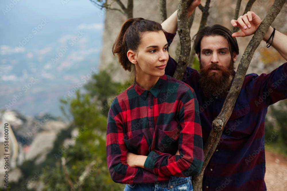 Portrait of stylishly dressed couple of hipsters posing in nature mountains landscape, handsome stylish man with beard and gorgeous brunette hair young woman, stylish couple in love posing outdoors