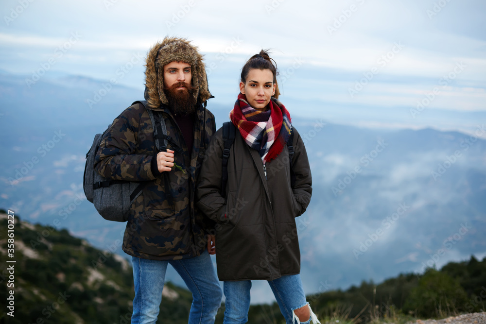 Backpackers standing on top of a mountain against foggy valley, portrait of two hikers with backpacks standing on mountain point with amazing foggy valley on background.