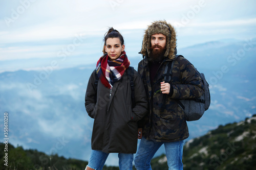 Portrait of two hikers with backpacks standing on mountain point with amazing foggy valley on background, backpackers standing on top of a mountain against foggy valley