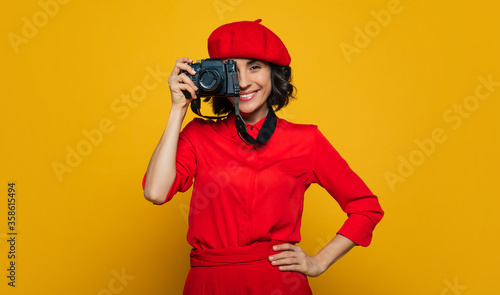 Nice big smiles, everybody! Half-length photo of a cute toothy smiling woman on her vacation, french style dressed, carrying a camera on a strap on her neck, ready to make a photo.
