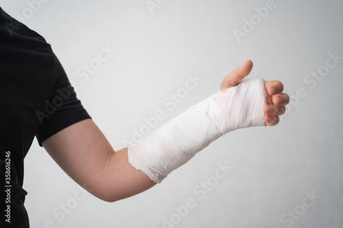 Quadro su tela A young man shows the injury of a broken arm in a plaster bandage on a white background