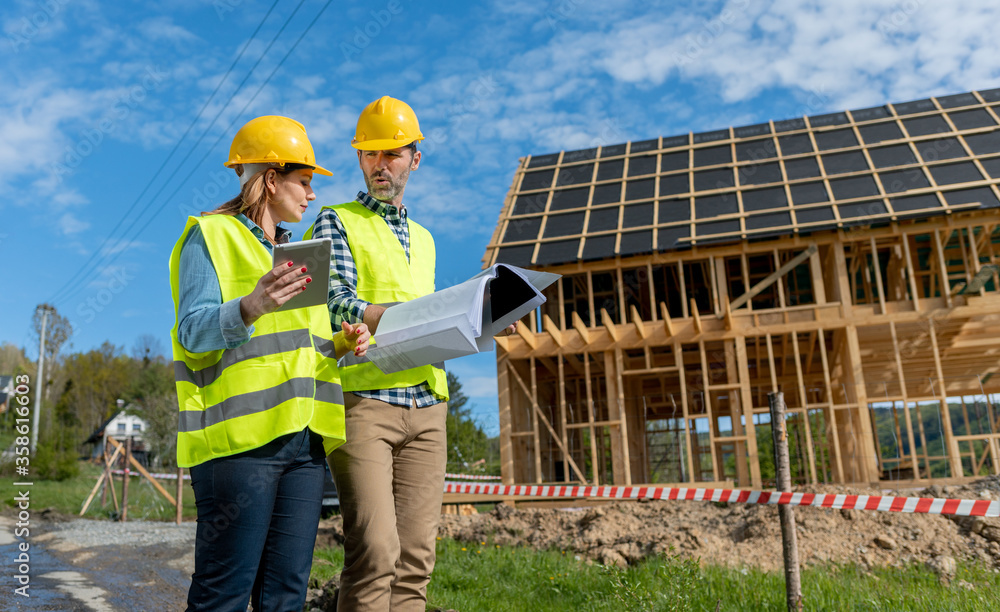 Engineers working on construction site holding blueprints of wood frame house Engineers working on construction site holding blueprints of wood frame house