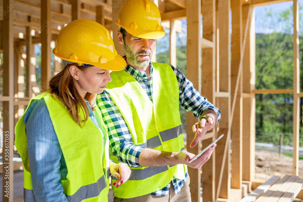 Engineers working on construction site holding blueprints of wood frame house Engineers working on construction site holding blueprints of wood frame house