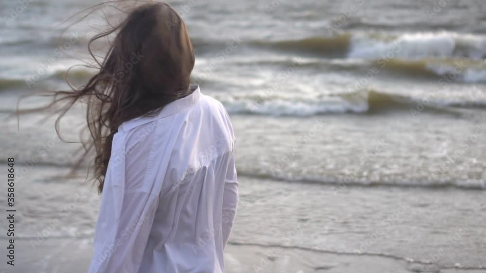 Playful young woman enjoying summer vacation at summer beach. Sensuous female with windswept hair is walking on beach at island wearing in a white shirt by sea. Playful young woman enjoying summer vacation at summer beach. Sensuous female with windswept hair is walking on beach at island wearing in a white shirt by sea.