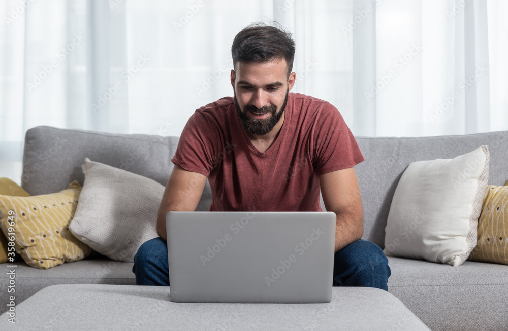 Young bearded freelance casual guy sitting on the sofa ant talking online through the laptop computer with a client about new job project for his company Young bearded freelance casual guy sitting on the sofa ant talking online through the laptop computer with a client about new job project for his company