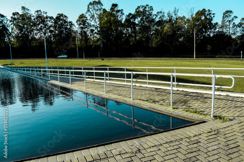 Piscina azul refletindo horizonte de árvores. Rampa com guarda-corpo. 