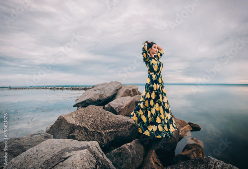 Woman in long dress standing on the rocks and looks at the sea