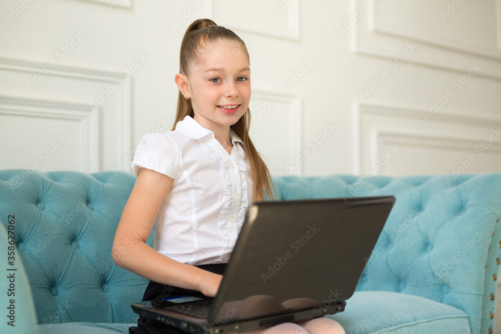 beautiful little teenager girl in a white shirt sits on a sofa with a laptop beautiful little teenager girl in a white shirt sits on a sofa with a laptop