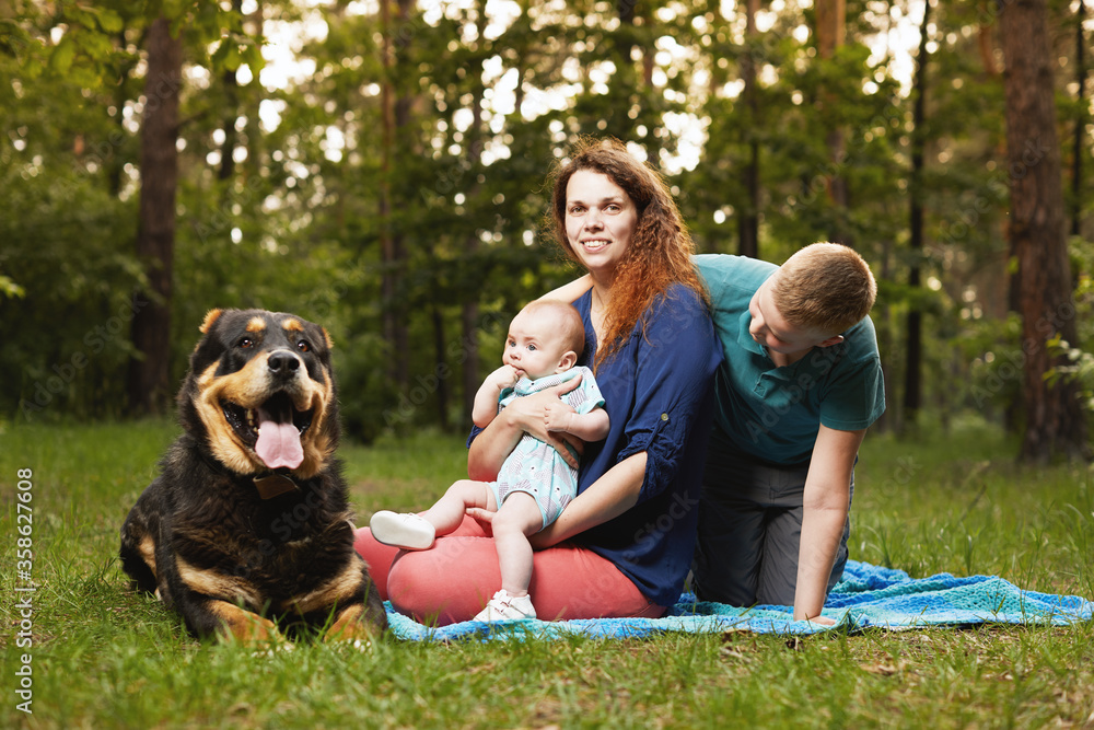 Mom relaxing on blanket with baby and son and big dog in the forest Mom relaxing on blanket with baby and son and big dog in the forest