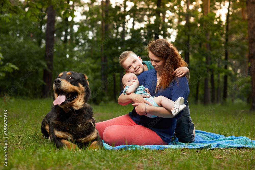 Mom relaxing on blanket with baby and son and big dog in the forest Mom relaxing on blanket with baby and son and big dog in the forest