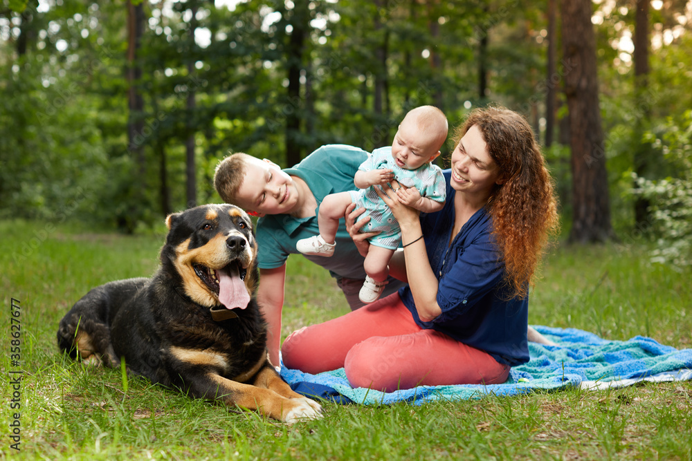 Mom relaxing on blanket with baby and son and big dog in the forest Mom relaxing on blanket with baby and son and big dog in the forest