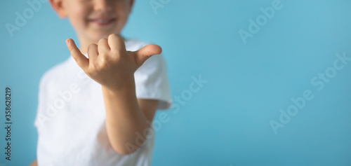 Little happy boy making a hang loose, Shaka hand sign. In studio blue background. © kieferpix