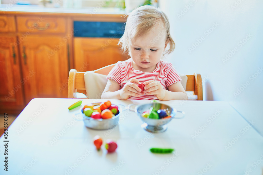 Adorable little girl playing with toy fruits and vegetables at home Adorable little girl playing with toy fruits and vegetables at home